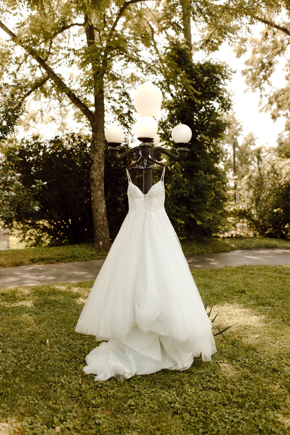An exquisite wedding dress delicately hanging on a light post in Mt. Sterling, Kentucky. The dress, bathed in soft light, radiates elegance and captures the enchanting atmosphere of the pre-wedding preparations in this picturesque location.