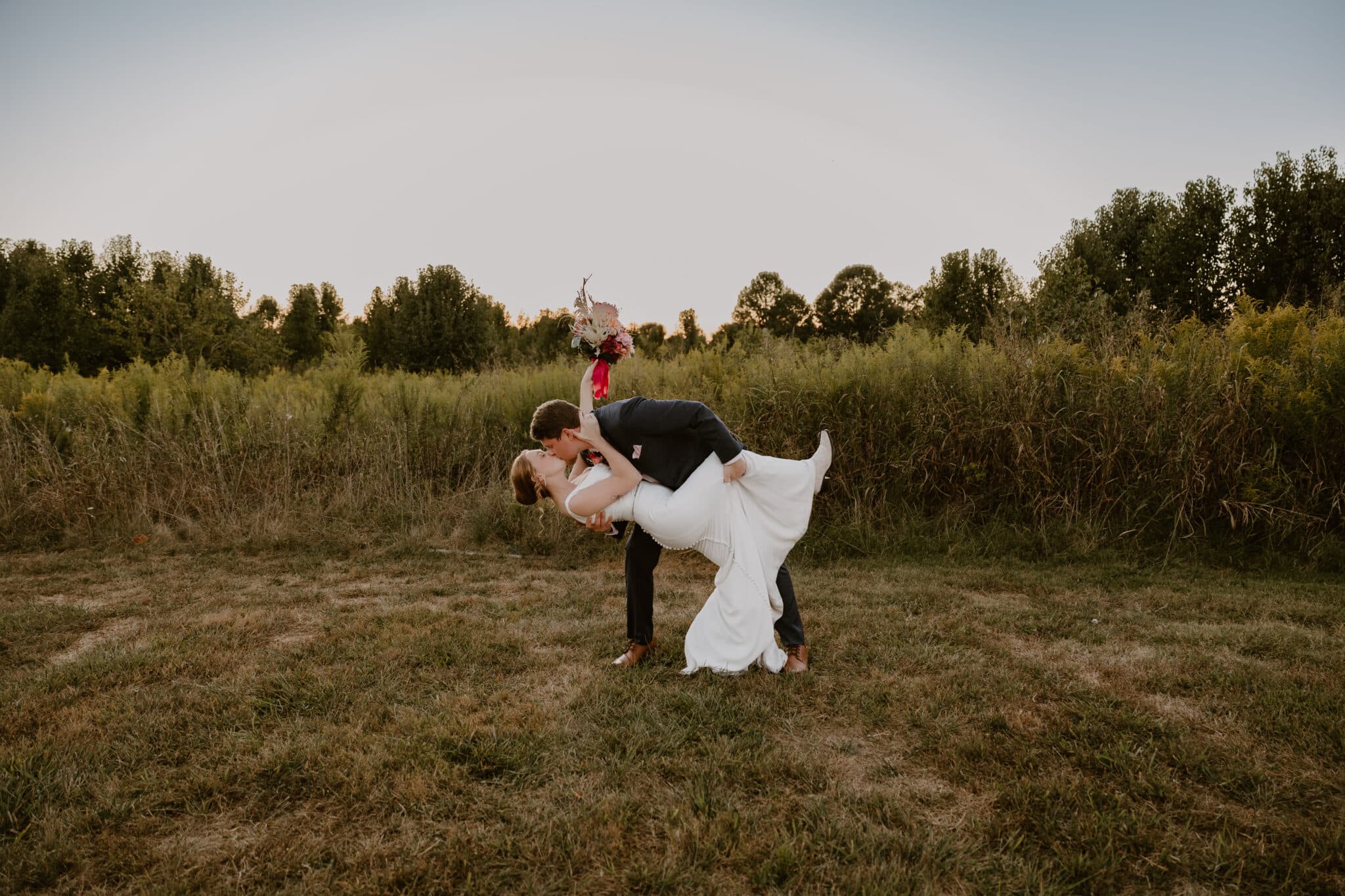 Groom dips bride for a romantic sunset kiss during their microwedding photoshoot, set against a warm and glowing sky.